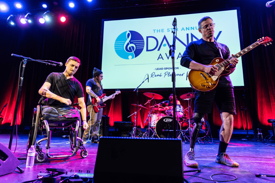 Photo of The Resilient performing at the 2024 Danny Awards. They are a four-piece, with a guitarist, drummer, bass, and singer. Three members of the band are amputees--two with prosthetics, with the singer using a wheelchair. 