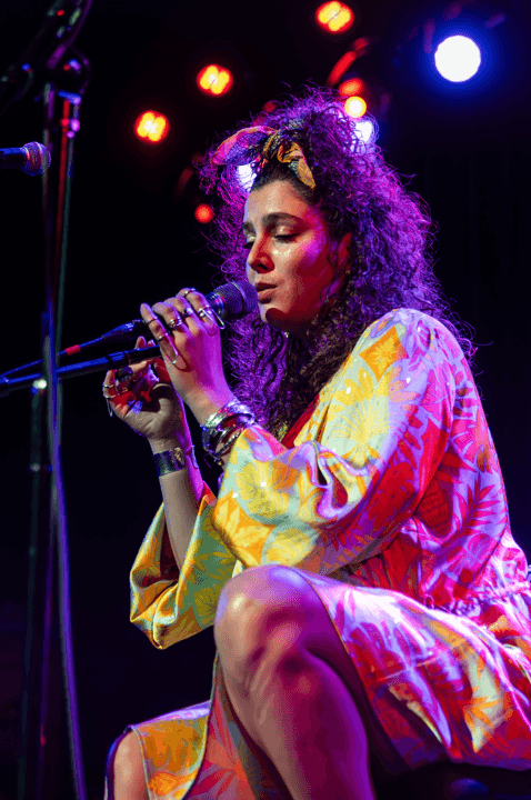 Photo of Ryth Lyon singing at the 2024 Danny Awards. She is sitting in a wheelchair, with long curly hair tied up with a ribbon. 