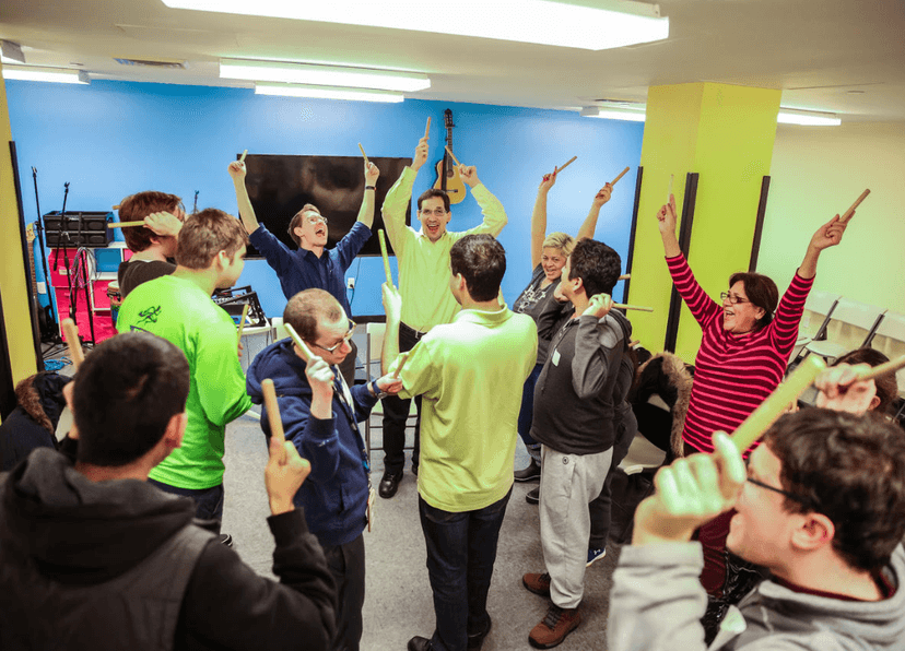 Photo of David teaching an in-person class. The members are in a circle, holding sticks in the air and smiling.