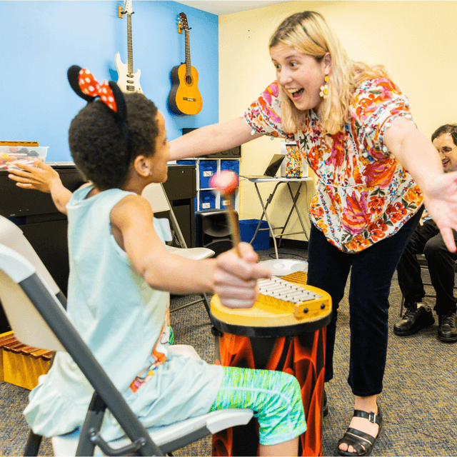 Photo of Stefani and a member with arms open facing each other around a bongo