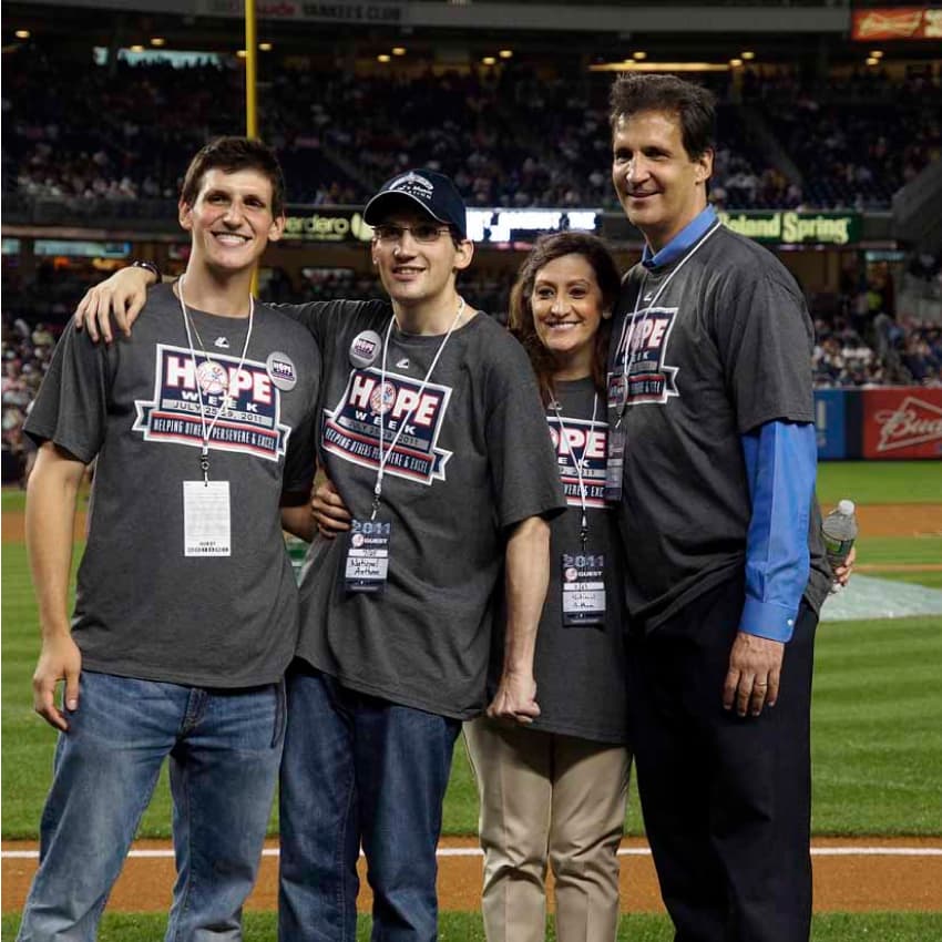 The Trush family stands on a baseball field with their arms around each other. They're wearing shirts for the New York Yankees' HOPE Week