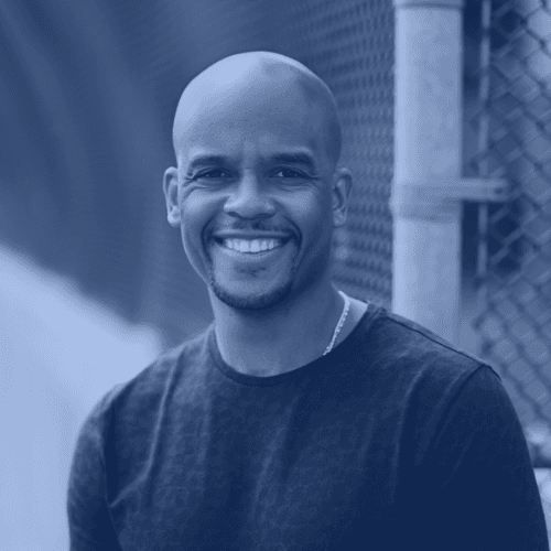 Portrait of Omar Grant, a black man in his late 30s to early 40s. He is smiling, has a goatee and a shaved head, and is wearing a t-shirt.